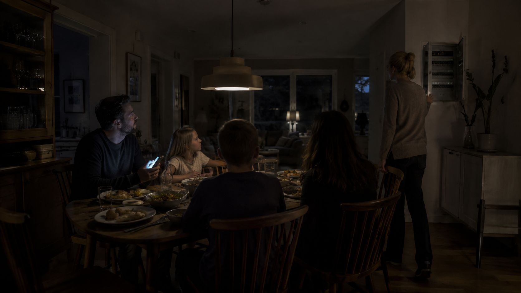 En familj äter middag i mörkret medan en kvinna kontrollerar elcentralen i ett hem i Danderyd.